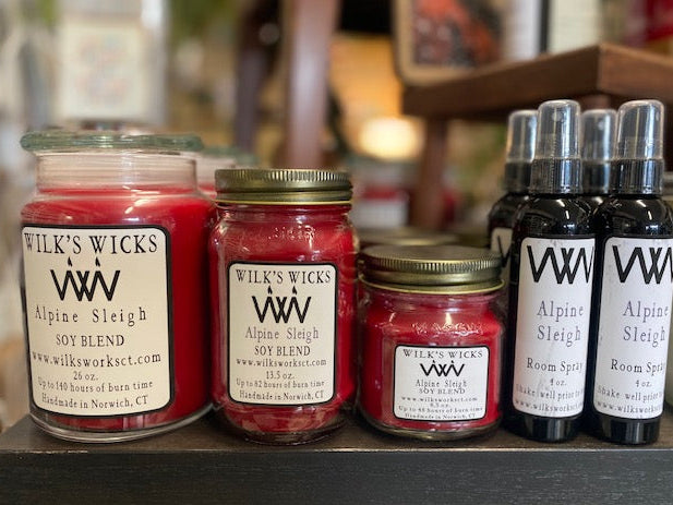 Jars and bottles of Wilk's Wicks Alpine Sleigh soy blend candles and room sprays on a shelf.